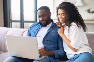 Afro-Amerikalı çift evde dizüstü bilgisayarla vakit geçiriyor.