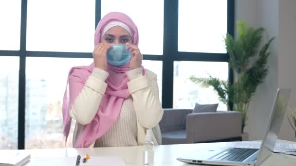 Femme musulmane portant hijab met masque médical sur le visage assis au bureau — Video