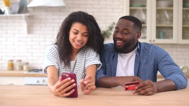 Boldog multiracionális pár okostelefont használ az otthoni online vásárláshoz — Stock videók