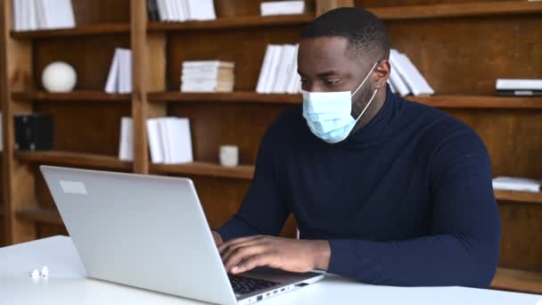 실내 노트북을 사용하여 의료 마스크를 쓰고 있는 아프리카 계 미국인 남성 근로자 — 비디오