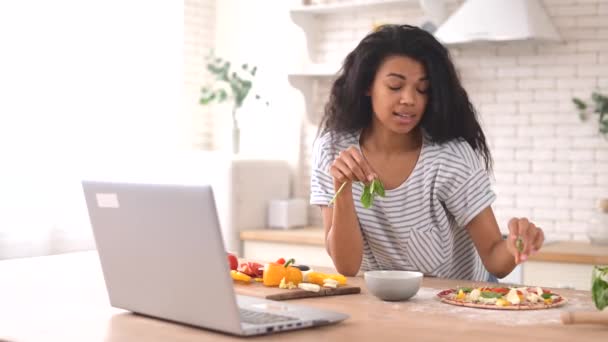 Affascinante donna birazziale guardando video tutorial di cucina sul computer portatile — Video Stock