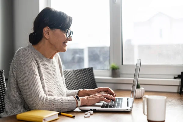 Charming senior woman using laptop at home for remote work