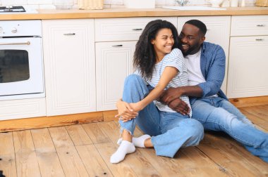 Evli çift mutfakta kucak kucağa oturuyor.