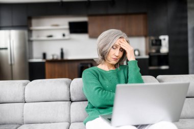 Evde dizüstü bilgisayar kullanan yaşlı bir kadın.