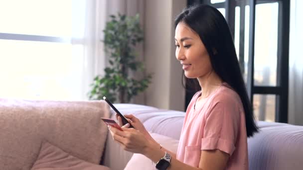 Çekici genç Asyalı bir kadın internetten alışveriş yapmak için akıllı telefon kullanıyor. — Stok video