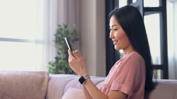 Una atractiva joven asiática mujer está utilizando un teléfono inteligente interior — Vídeos de Stock