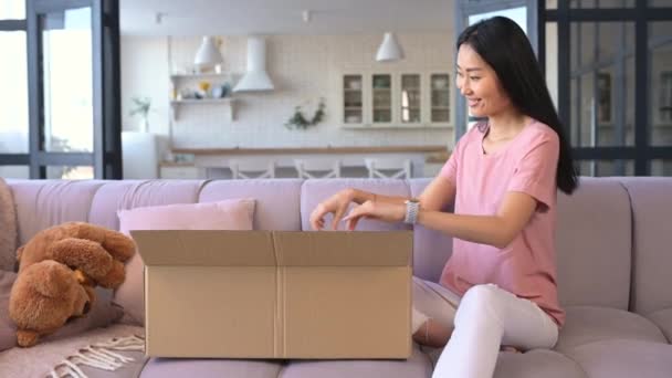 Una atractiva joven asiática mujer desempacando una caja de paquetes — Vídeo de stock