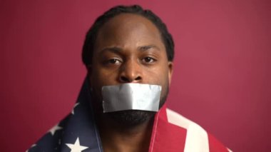 Dili tutulmuş, ağzı kapalı, kırmızı arka planda izole edilmiş Afro-Amerikalı bir adam.