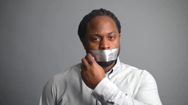 Афроамериканець знімає стрічку з рота на сірому фоні — стокове відео