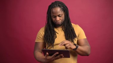 Kırmızı arka planda izole edilmiş tablet kullanan Afro-Amerikalı adam.