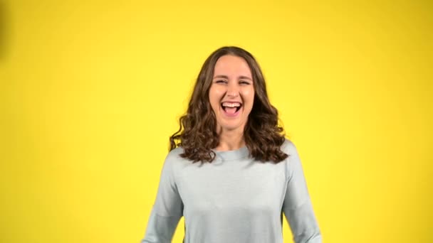 Приваблива кучерява молода жінка піднімає руки вгору ізольовано на жовтому — стокове відео