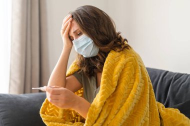 Yüz maskesi takan genç bir kadın evde kendini hasta hissediyor.