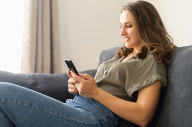 Evde akıllı telefon kullanan çekici kıvırcık kadın.