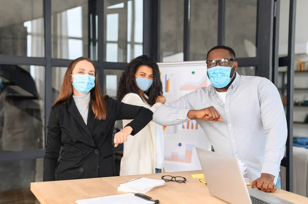 Multiracial colleagues wearing masks greeting each other with elbows