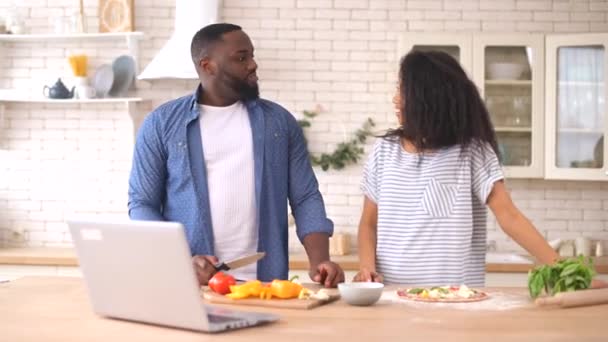 Feliz pareja multirracial preparando la comida juntos delante de un ordenador portátil — Vídeos de Stock