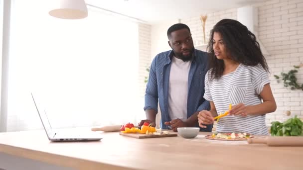 Feliz pareja multirracial preparando la comida juntos delante de un ordenador portátil — Vídeos de Stock