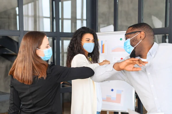 Colleagues in masks greeting each other bumping elbows at workplace