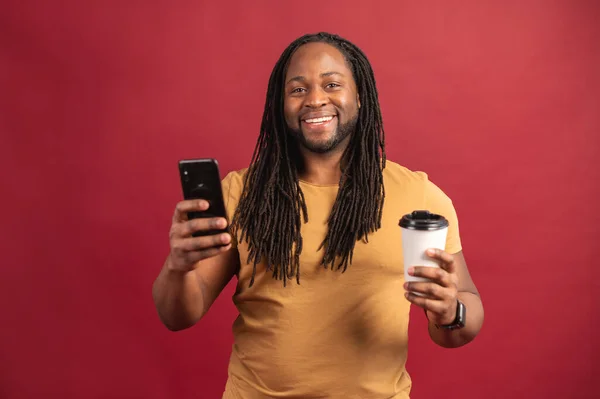 Foto av glad svart man med hjälp av smartphone och takeaway cup — Stockfoto
