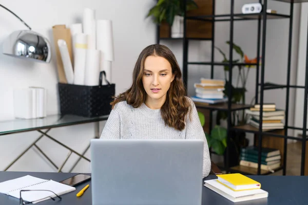 Впевнена молода жінка працює з ноутбуком в офісі — стокове фото
