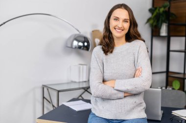 Ofiste kollarını kavuşturmuş gülümseyen kadın.