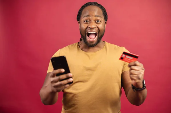 Gelukkig Afrikaans man met credit card en mobiele telefoon in zijn handen — Stockfoto