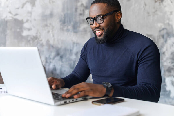 Уверенный афроамериканец, пользующийся ноутбуком в офисе