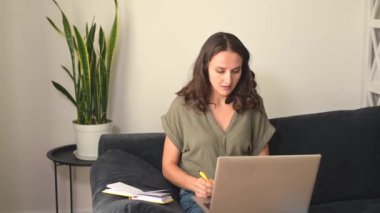 Bilgisayarlı odaklanmış genç bir kadın not alıyor.