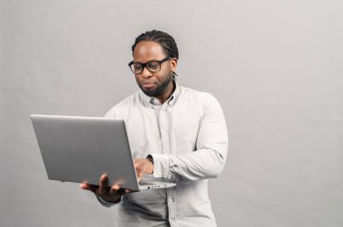 Akıllı Afro-Amerikalı adam, gri üzerine izole edilmiş bir laptop kullanıyor.