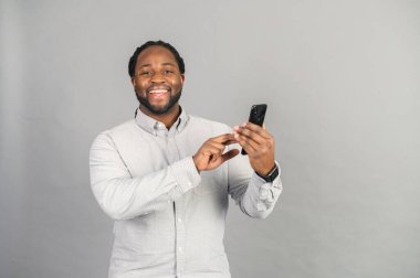 Gri yolda izole edilmiş akıllı telefonlu bir adamla gülümseyen Afro-Amerikalı.