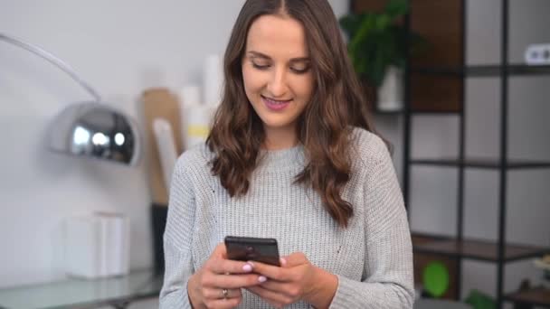 笑顔の若い女性がオフィスでスマートフォンを使用しています — ストック動画