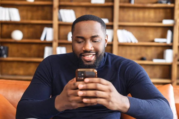 Αφροαμερικάνος κάθεται με το τηλέφωνο στα χέρια παθιασμένος με κάτι — Φωτογραφία Αρχείου