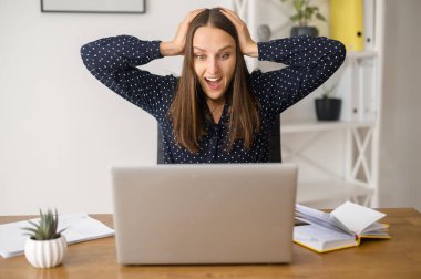 Şaşırmış kadın dizüstü bilgisayarın önünde oturuyor.