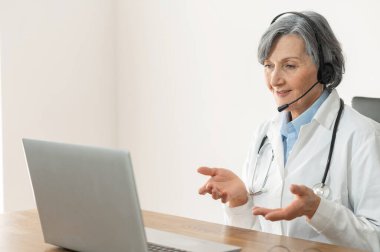 Masada oturan kulaklıklı kıdemli bayan doktor.