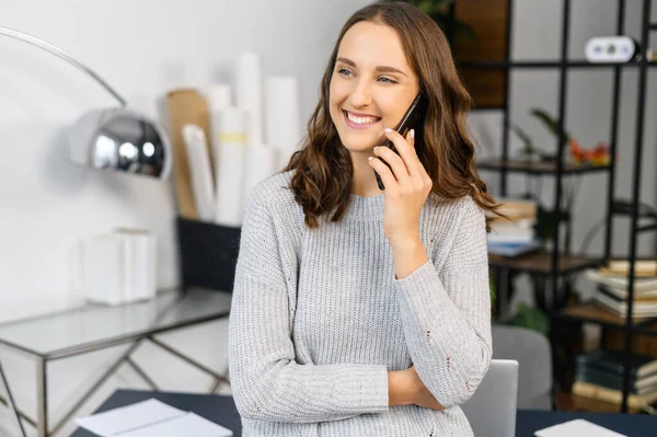 Gülümseyen kadın telefonla konuşur ve kameraya bakar.