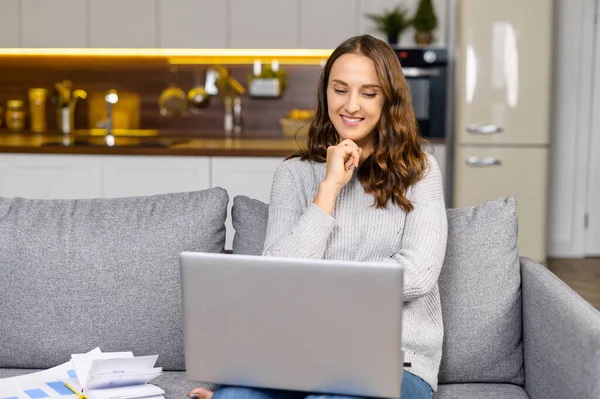 Gelukkig vrouw zit op de comfortabele bank met een laptop op de ronden — Stockfoto