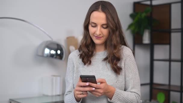 Sorrindo jovem mulher está usando smartphone no escritório — Vídeo de Stock