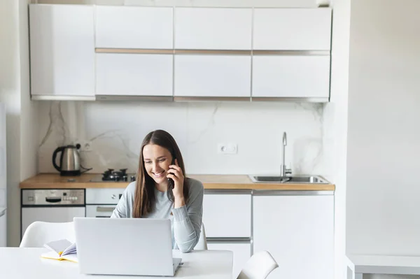 Lächelnde und positive junge Frau spricht über Smartphone und Laptop — Stockfoto