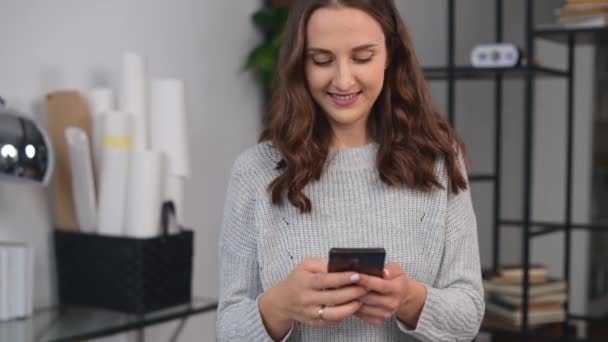 Lächelnde junge Frau nutzt Smartphone im Büro — Stockvideo