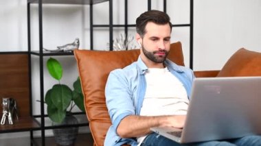 Evde dizüstü bilgisayar kullanan, sıradan bir tişört giyen odaklanmış bir adam.