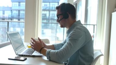 Kendine güvenen bir erkek işçi elinde dizüstü bilgisayarla masada oturuyor ve uzaktan çalışıyor.