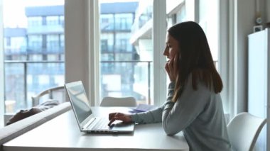 Genç bir kadın akıllı telefonda konuşur ve klavyede daktilo çalar.