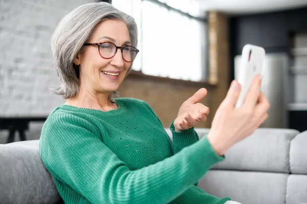 Hermosa mujer mayor usando smartphone para videollamadas en casa —  Fotos de Stock