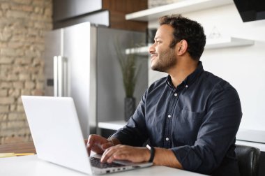 Evden uzakta bilgisayarla çalışan gülümseyen Hintli adam.