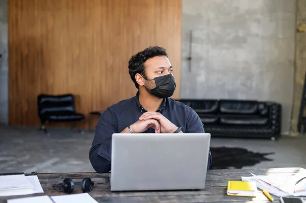 Portrait of worried indian man in protective facial mask in the workplace