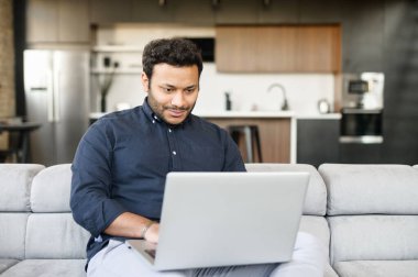 Gülümseyen, melez, serbest çalışan adam dizüstü bilgisayar kullanıyor.