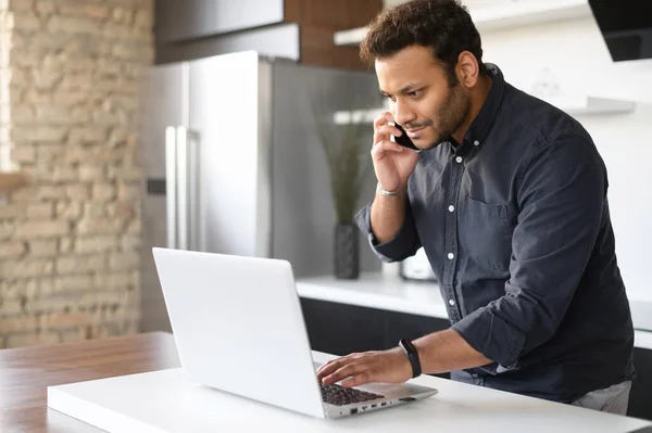 Ragazzo indiano sta parlando sullo smartphone e utilizzando il computer portatile a casa — Foto Stock