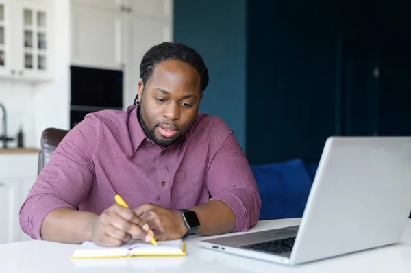 Intelligent and smart African-American male entrepreneur using laptop computer and takes notes