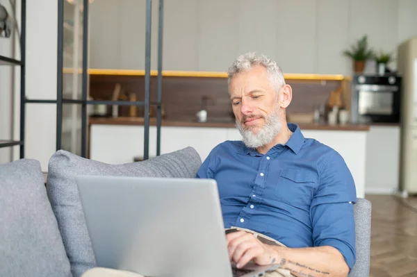 Bärtiger Mann mittleren Alters legt sich mit Laptop auf die Couch — Stockfoto