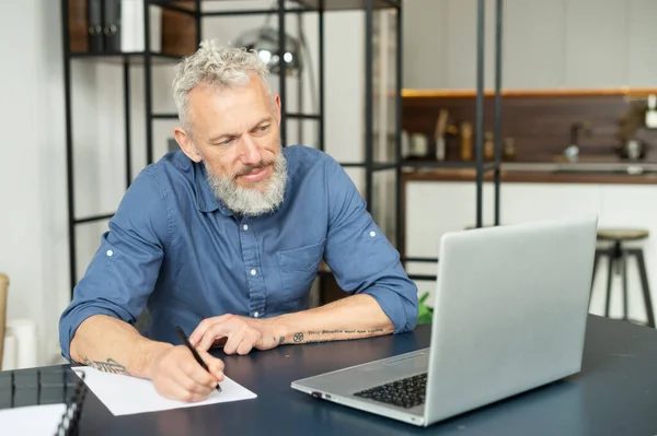 Moderno uomo tatuato barbuto di mezza età che lavora con un computer portatile in home office — Foto Stock