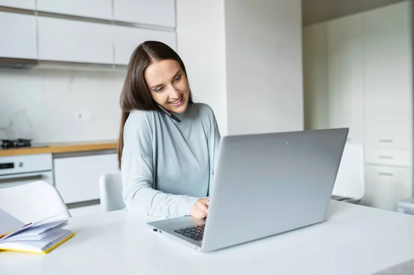 Mulher ocupada segura um smartphone com um ombro e digitação no teclado do laptop — Fotografia de Stock